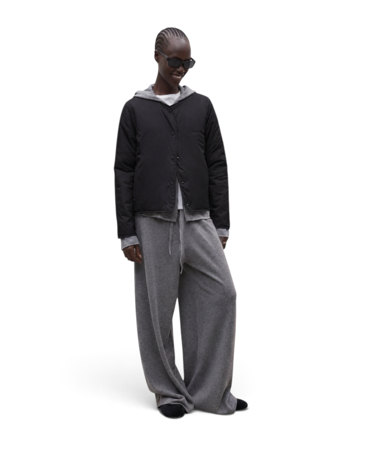 Modella indossa la giacca nera Monica di DevidLabel con cappuccio grigio, abbinata a pantaloni ampi in stile casual.