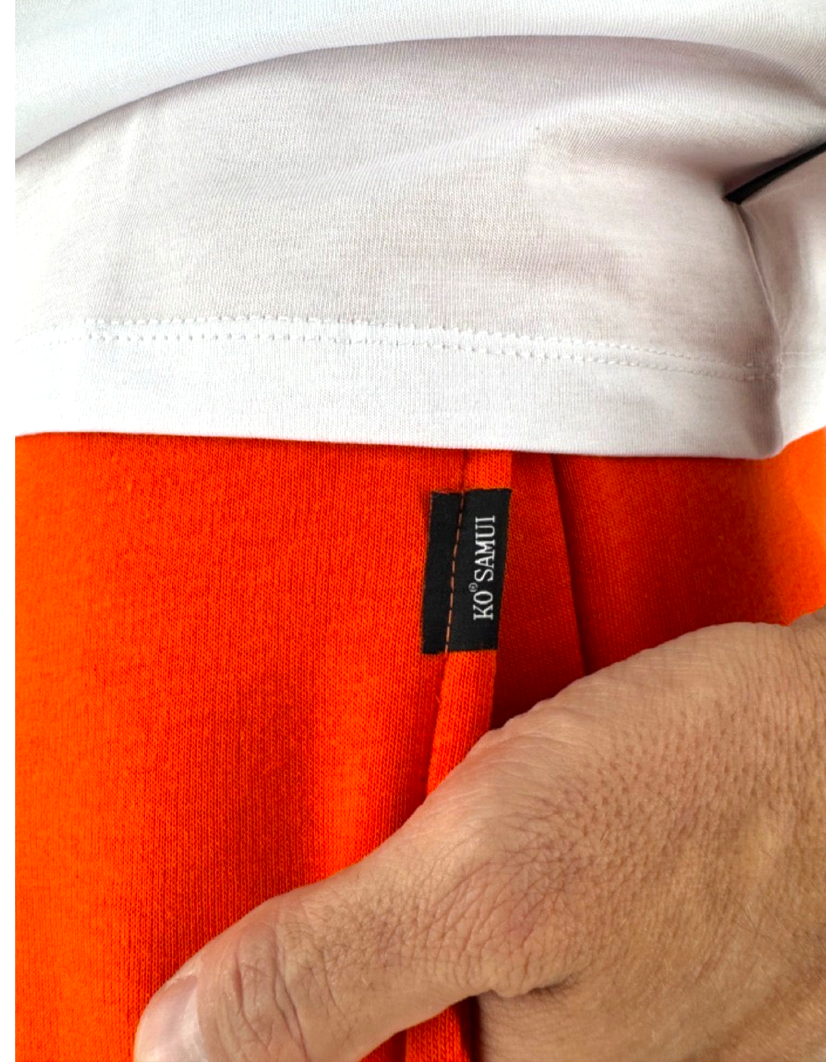 Dettaglio dei pantaloni in misto cotone arancione Ko Samui con etichetta Ko Samui e t-shirt bianca