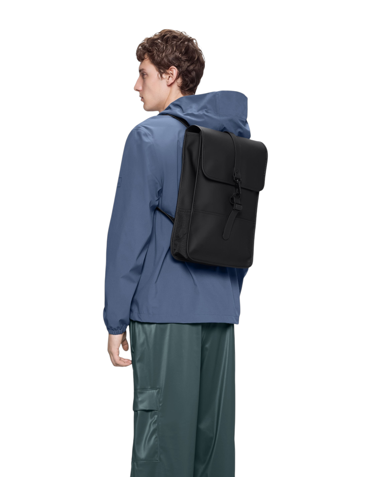Modello indossa zaino nero impermeabile Rains Backpack Mini di DevidLabel su giacca blu e pantaloni verdi