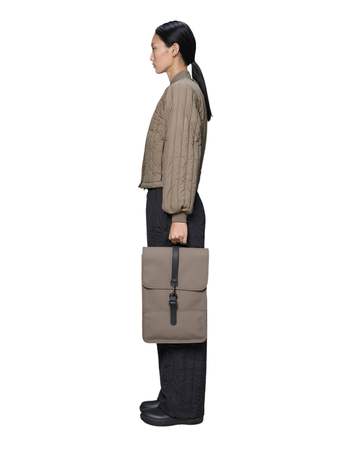 Modella di profilo indossa lo zaino Rains Backpack Mini color Cinder in PU impermeabile, venduto da DevidLabel.