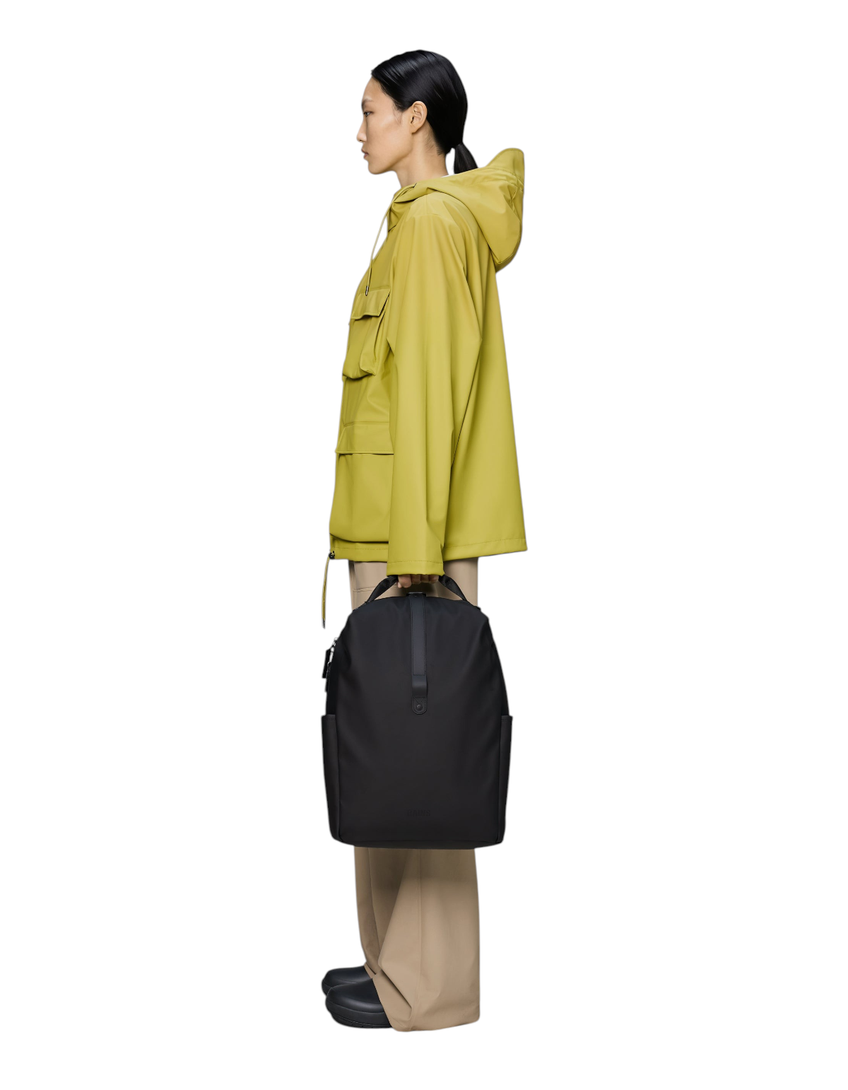 Modella di profilo indossa zaino nero Rains Clip Front Backpack in tessuto impermeabile con chiusura a clip