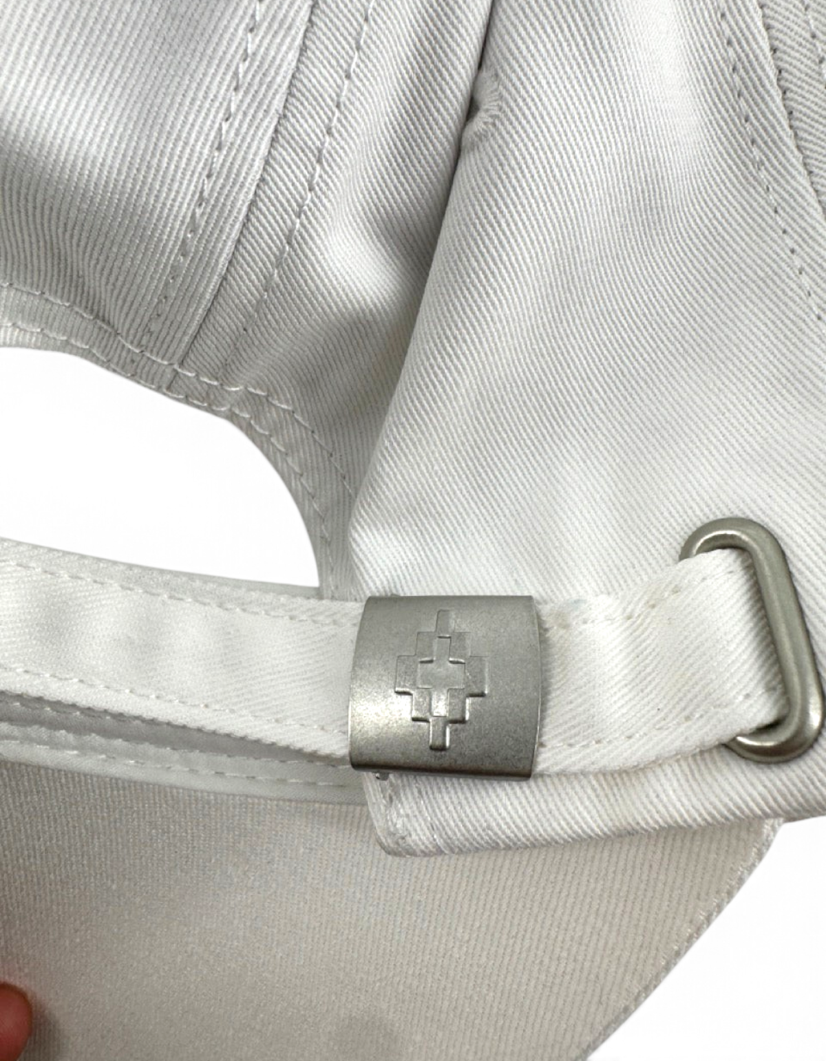 Dettaglio della fibbia metallica con logo inciso sul retro del cappellino DevidLabel in cotone bianco