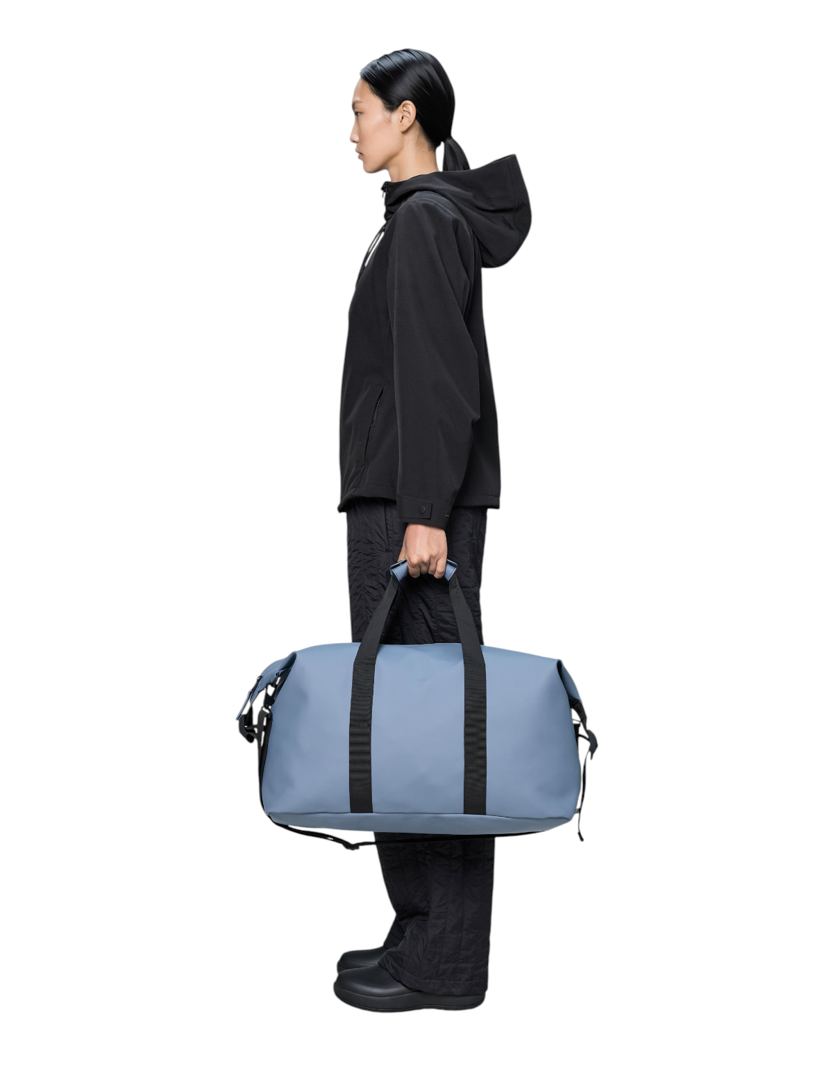 Modella che indossa un completo nero mentre tiene il borsone impermeabile Rains Hilo Weekend Bag color Blue Dusk