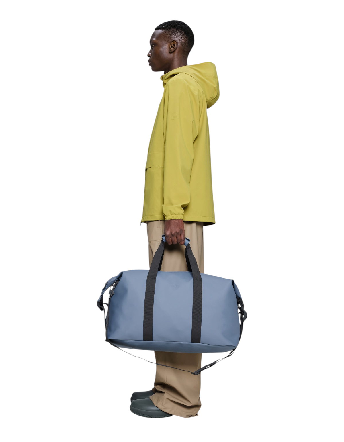 Modello indossa giacca gialla e tiene il borsone impermeabile DevidLabel Rains Hilo Weekend Bag color Blue Dusk