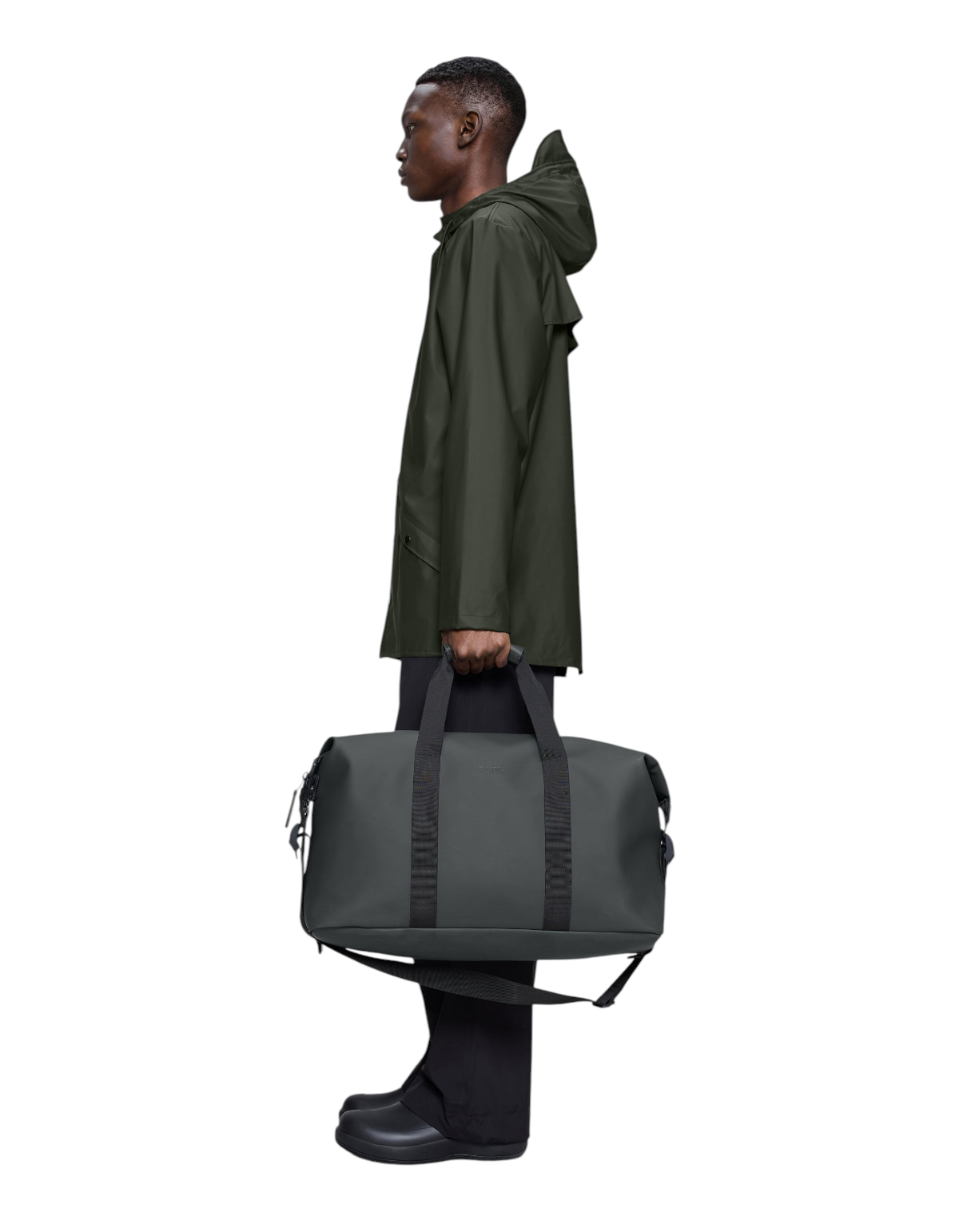 Modello indossa impermeabile scuro mentre tiene il borsone DevidLabel Rains Hilo Weekend Bag grigio scuro in mano