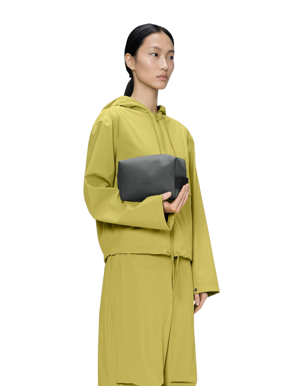 Modella che indossa un completo giallo tiene in mano la borsa da toilette DevidLabel Rains Wash Bag Small grigio scuro