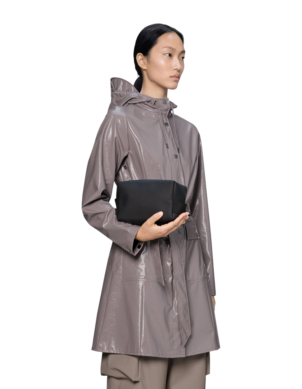 Modella che tiene in mano la Wash Bag Small nera di Rains, beauty case impermeabile dal design minimalista