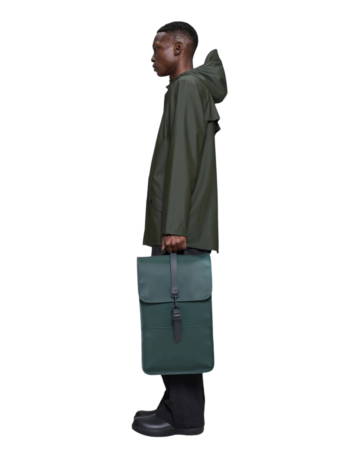 Modello indossa zaino impermeabile Rains Backpack Mystique verde scuro con chiusura a gancio, vista laterale